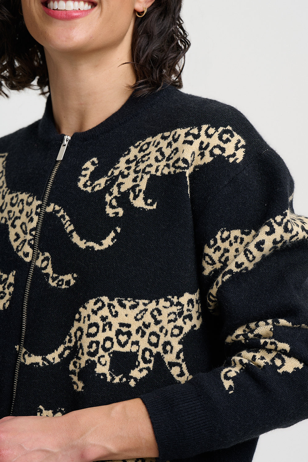 A close-up of a person wearing a black knit zip-up sweater with large beige leopard prints across the front and sleeves.