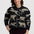 A woman wearing a black zip-up knit sweater with a beige leopard print pattern, paired with dark burgundy pants, against a light gray studio background.