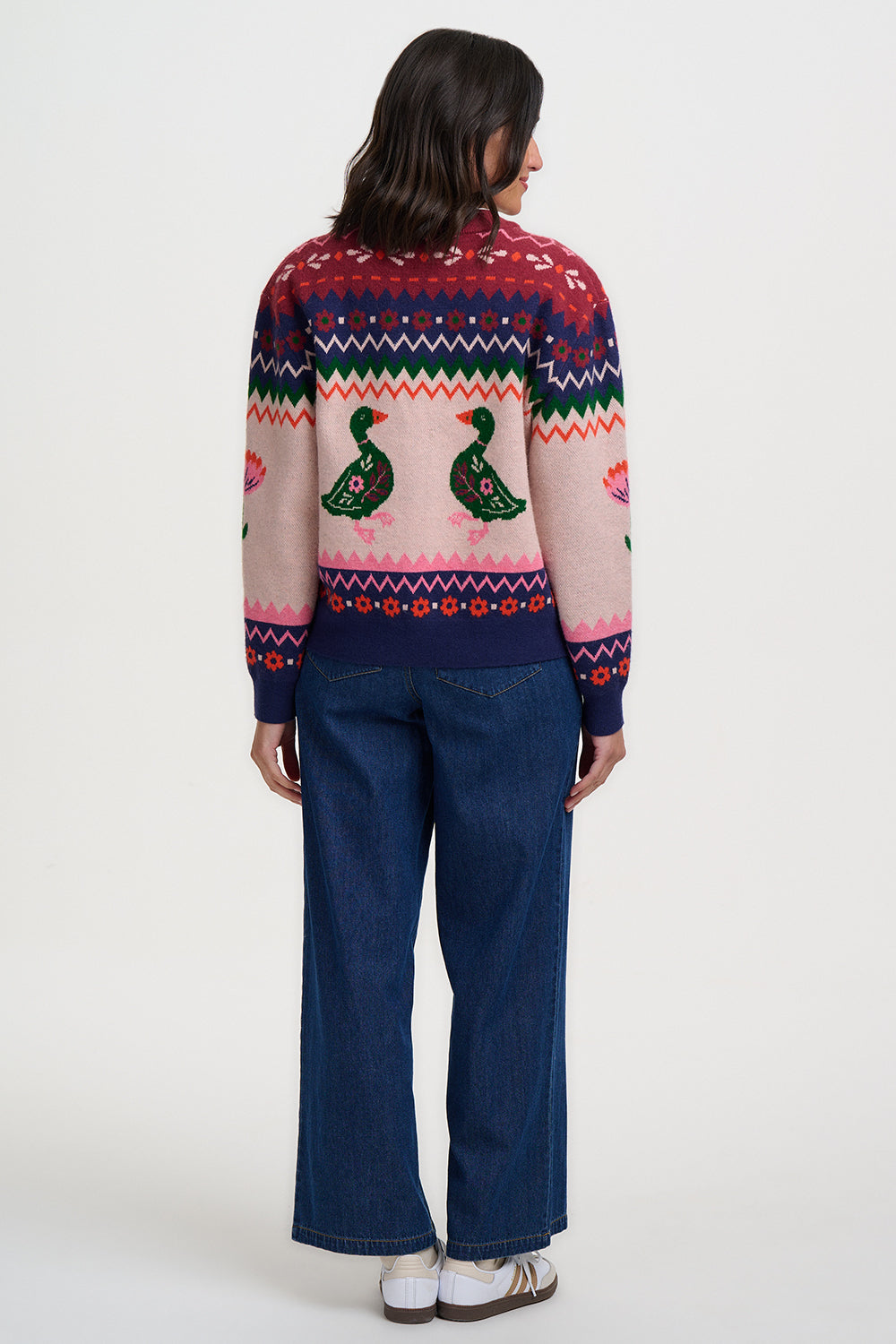 Person wearing a colorful sweater with duck design and blue jeans on a white background