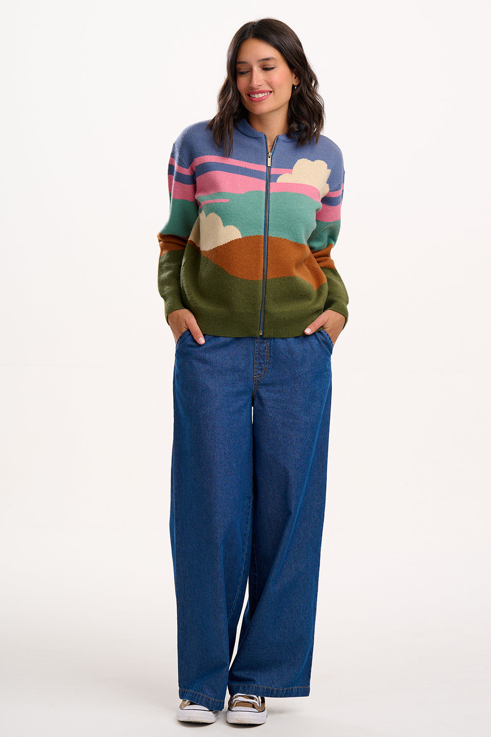 Woman wearing a colorful zip-up sweater and blue jeans on a white background