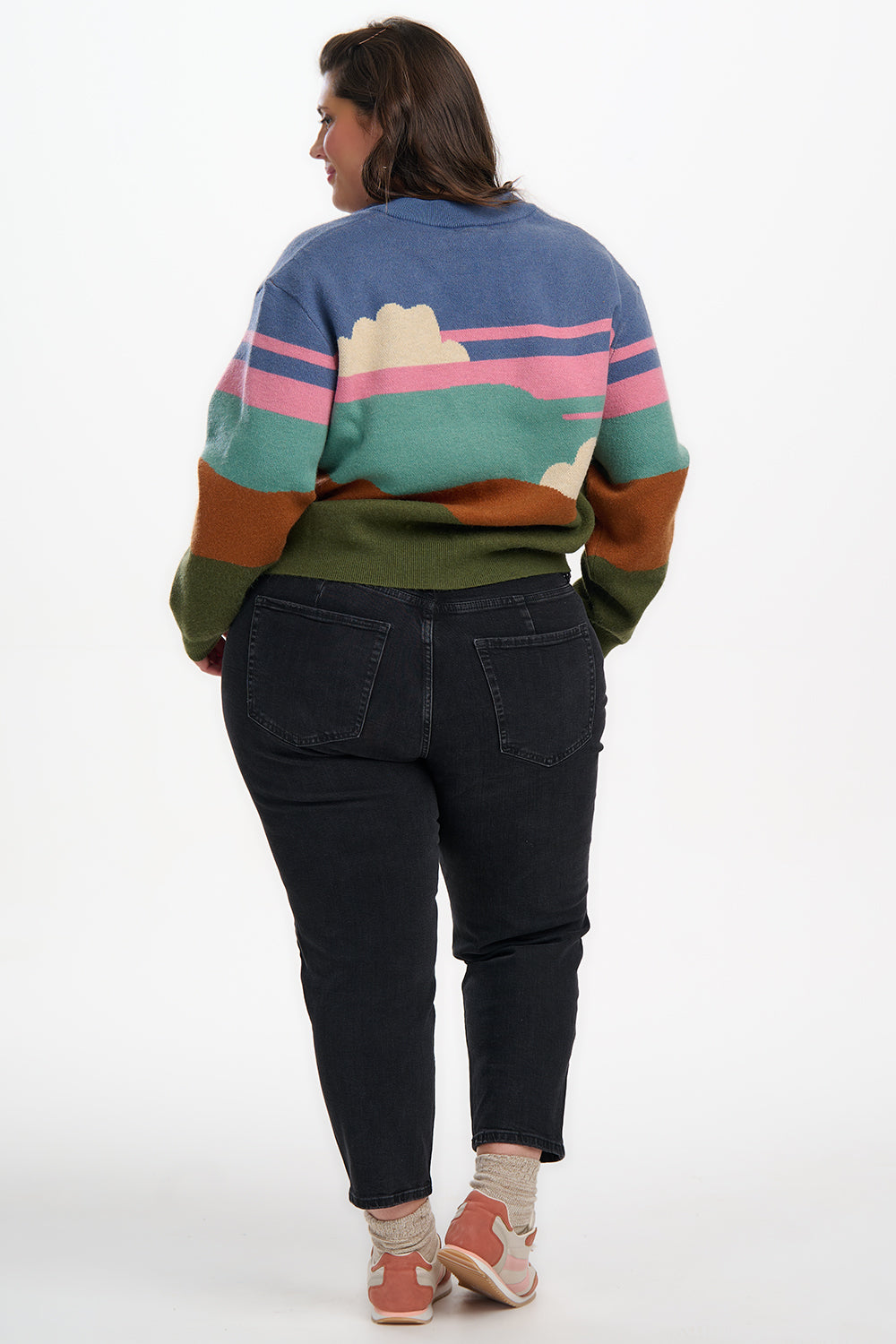 Person wearing a colorful sweater with a mountain design and black pants on a white background