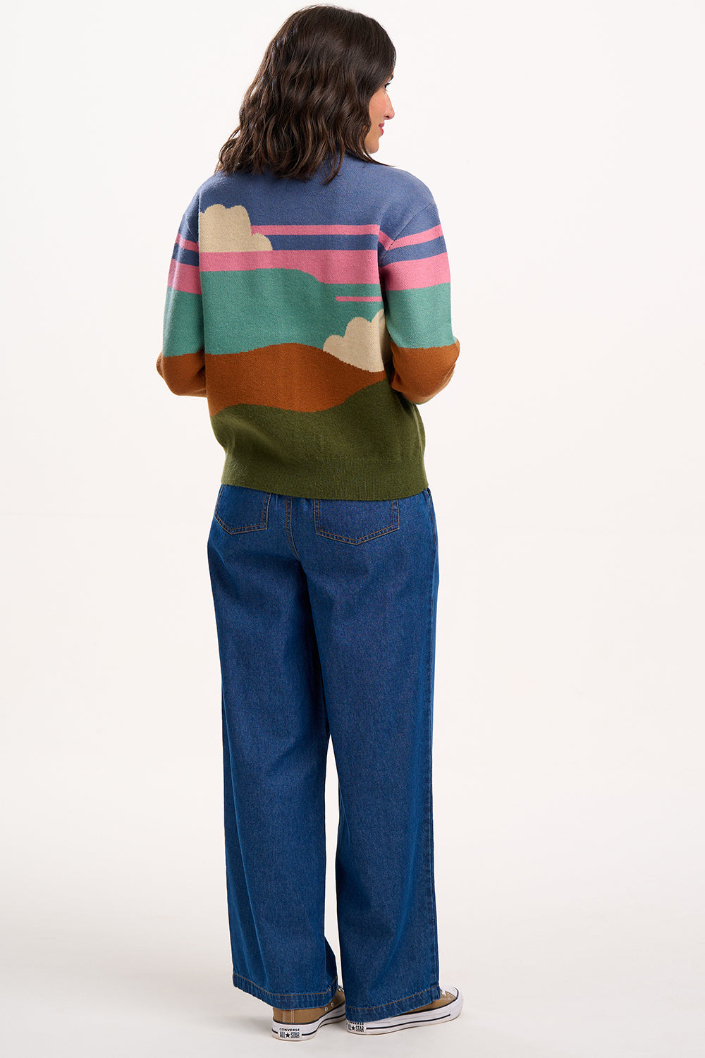 Person wearing a colorful sweater with abstract patterns and blue jeans on a white background