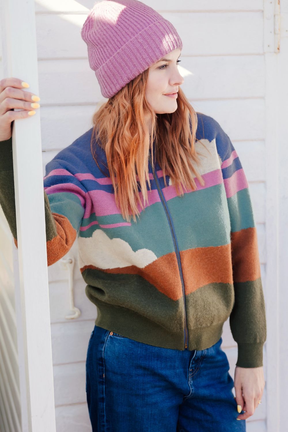 Person wearing a colourful sweater with a striped pattern and a purple beanie.