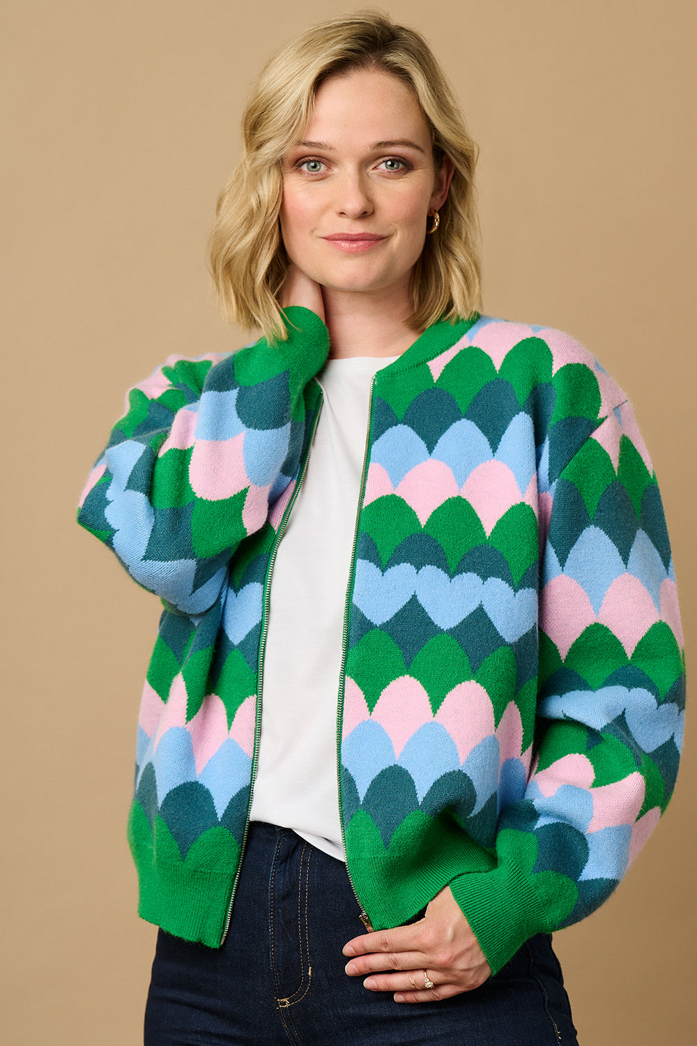 A model wearing a multicoloured knitted bomber jacket with a heart scallop pattern in green, blue, and pink.
