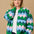 A model wearing a multicoloured knitted bomber jacket with a heart scallop pattern in green, blue, and pink.