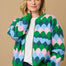 A model wearing a multicoloured knitted bomber jacket with a heart scallop pattern in green, blue, and pink.
