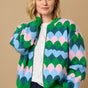 A model wearing a multicoloured knitted bomber jacket with a heart scallop pattern in green, blue, and pink.