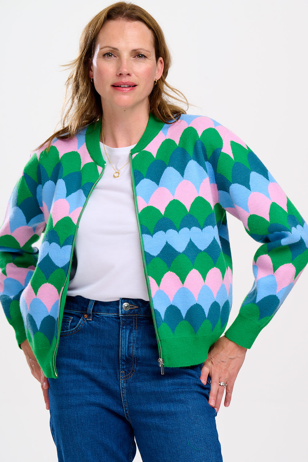 A model wearing a multicoloured knitted bomber jacket with a heart scallop pattern in green, blue, and pink.