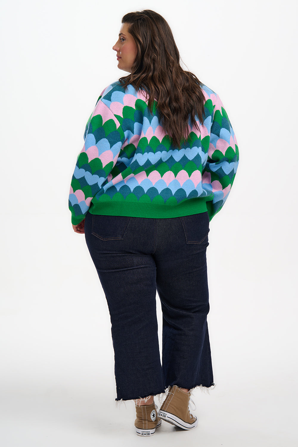 Person wearing a colorful patterned sweater and dark jeans on a white background