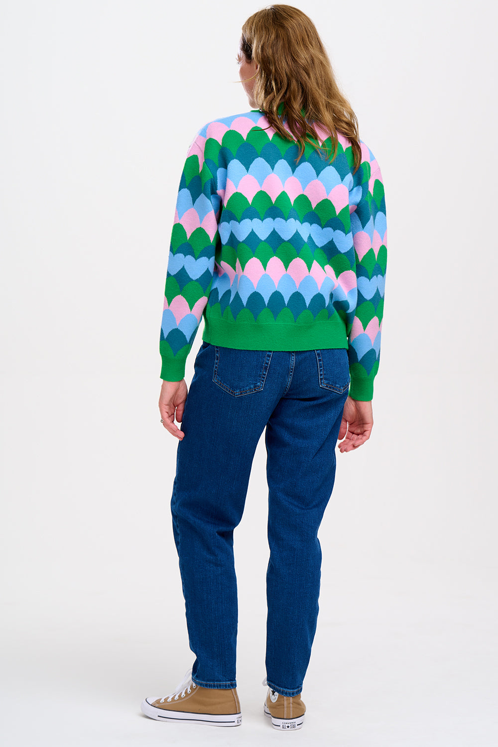 A model wearing a multicoloured knitted bomber jacket with a heart scallop pattern in green, blue, and pink.
