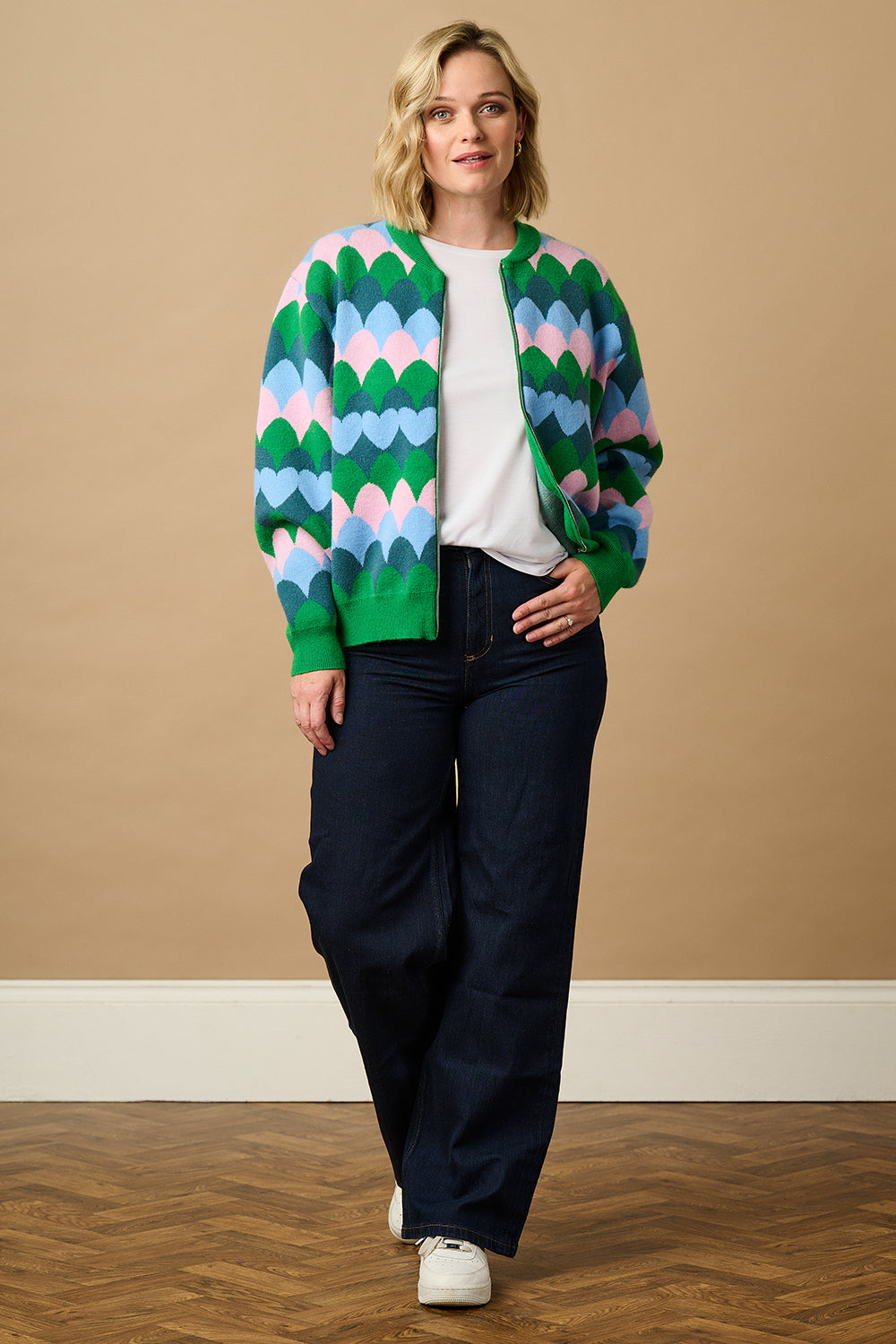 A model wearing a multicoloured knitted bomber jacket with a heart scallop pattern in green, blue, and pink.