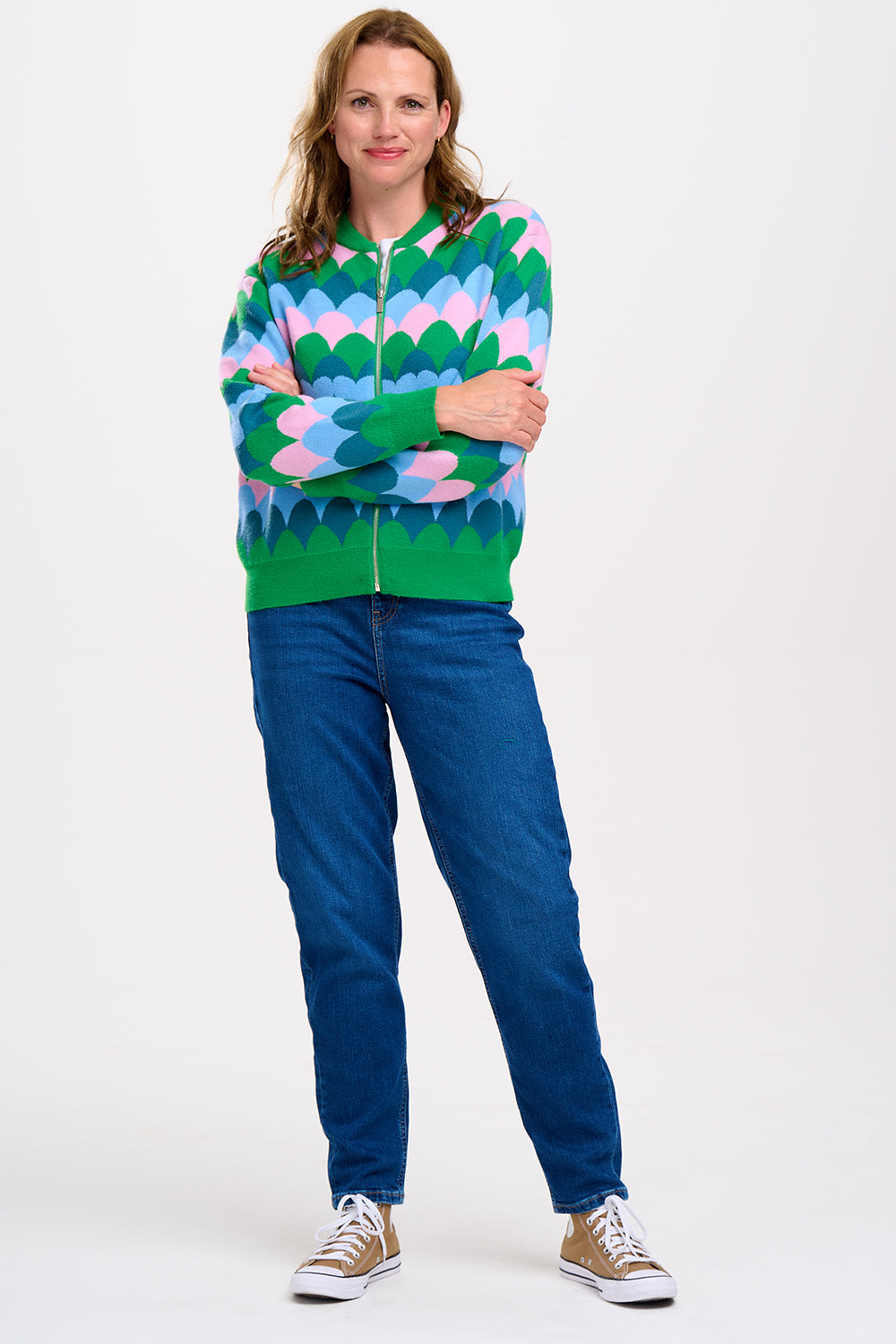 A model wearing a multicoloured knitted bomber jacket with a heart scallop pattern in green, blue, and pink.
