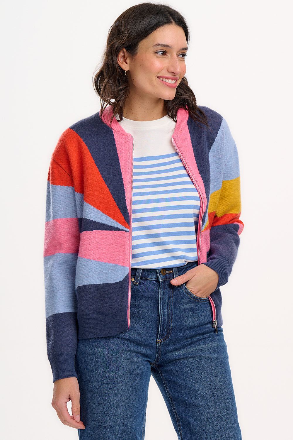 A woman wears a multicoloured knitted bomber jacket with a geometric pattern featuring shades of navy, blue, orange, pink, and mustard.