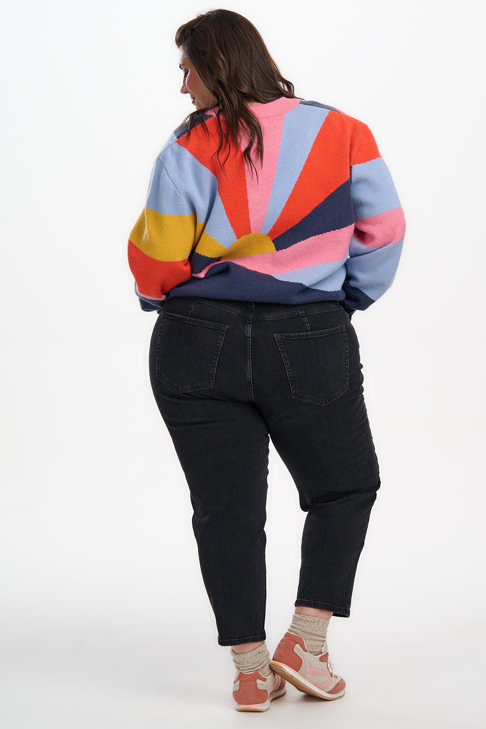 Person wearing a colorful striped sweater and black pants on a white background