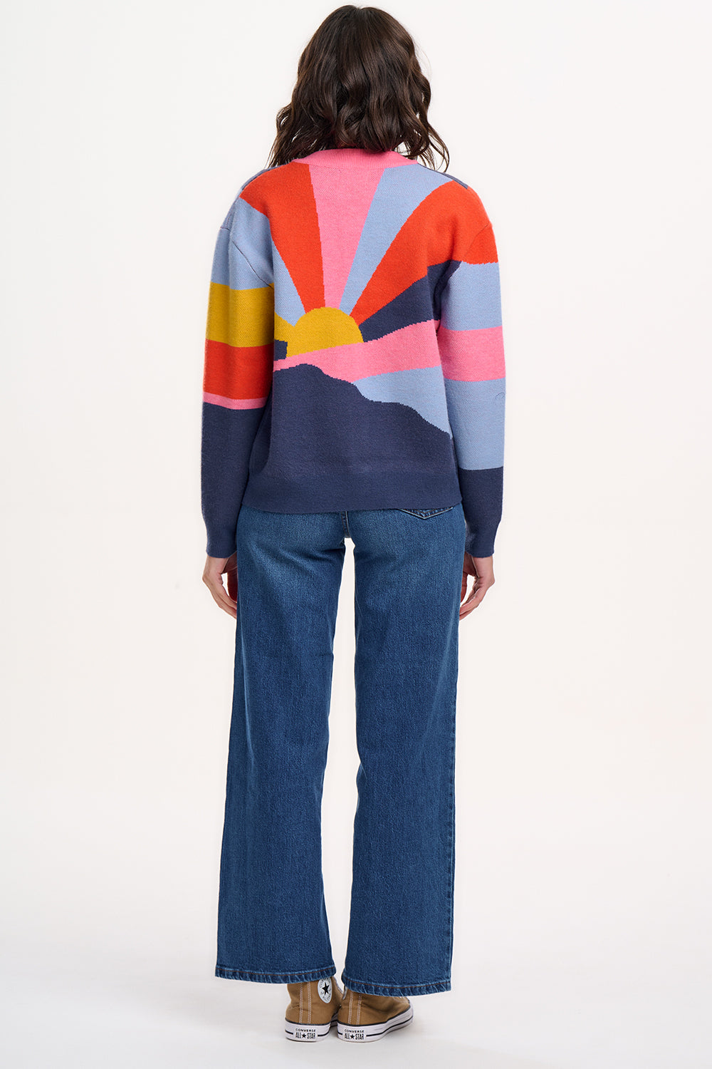 A woman wears a multicoloured knitted bomber jacket with a geometric pattern featuring shades of navy, blue, orange, pink, and mustard.
