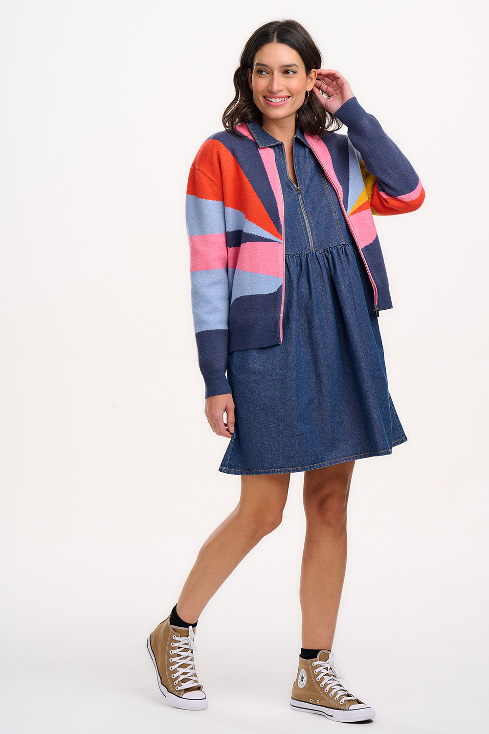 A woman wears a multicoloured knitted bomber jacket with a geometric pattern featuring shades of navy, blue, orange, pink, and mustard.