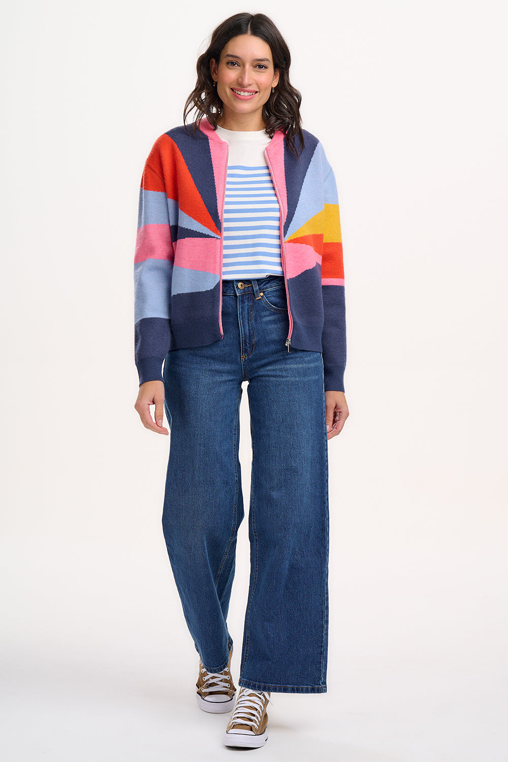 A woman wears a multicoloured knitted bomber jacket with a geometric pattern featuring shades of navy, blue, orange, pink, and mustard.