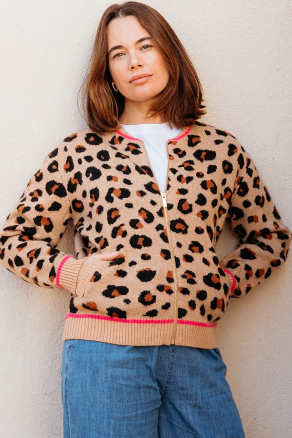 Woman wearing a leopard print cardigan with pink trim against a light background