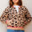 Woman wearing a leopard print cardigan with pink trim against a light background