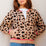 Woman wearing a leopard print cardigan with pink trim against a light background