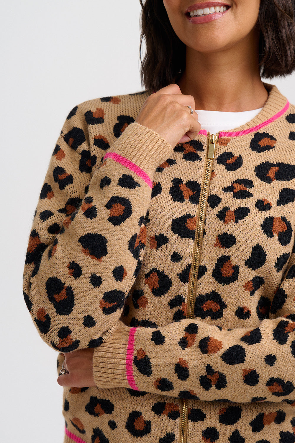 A close-up of a woman wearing a beige knit zip-up sweater with a black and brown leopard print pattern, featuring bright pink trim and a gold zipper.