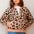Woman wearing a leopard print cardigan with pink trim against a light background