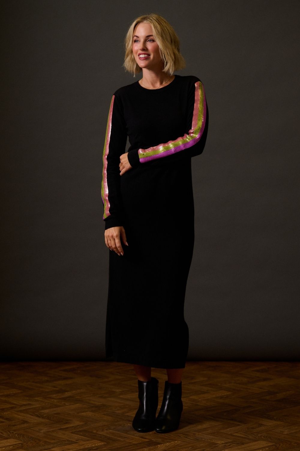 Woman wearing a black dress with colorful arm details against a dark background