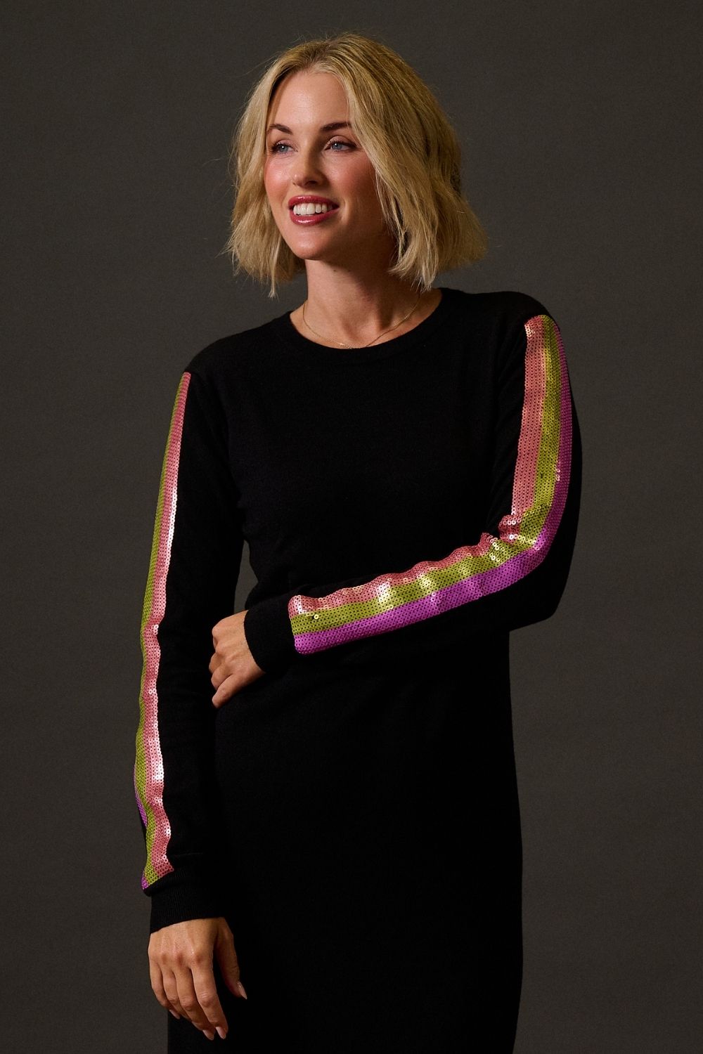 Woman wearing a black dress with pink and green arm sleeves against a dark background