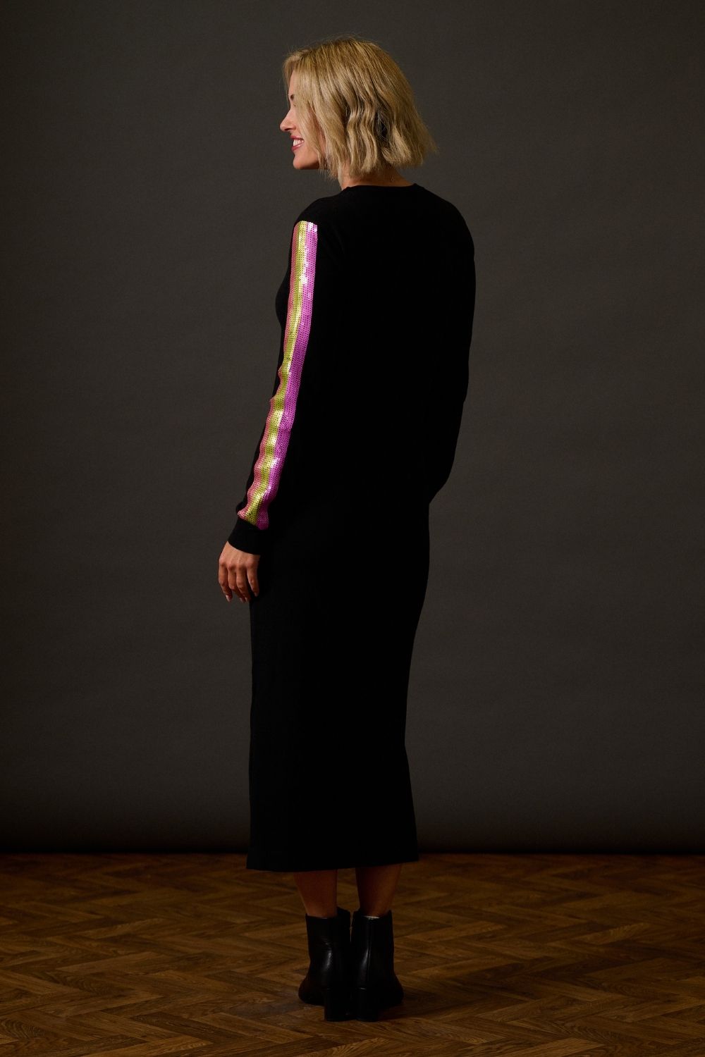 Woman wearing a black dress with colorful arm sleeves against a dark background