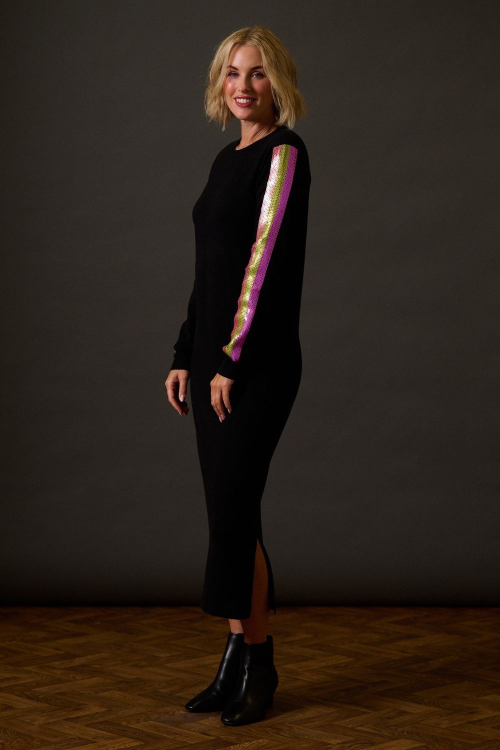 Woman wearing a black dress with colorful stripes against a dark background