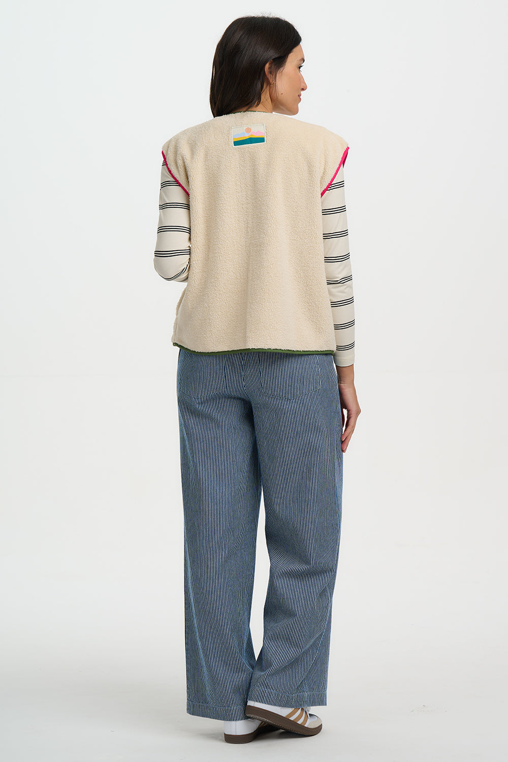 Person wearing a beige vest with colorful accents and blue pants on a white background