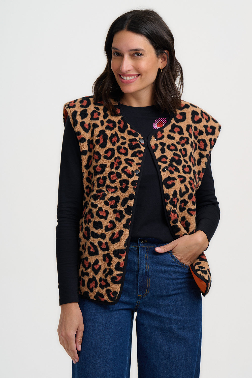 Woman wearing a leopard print vest over a black top and blue jeans on a white background