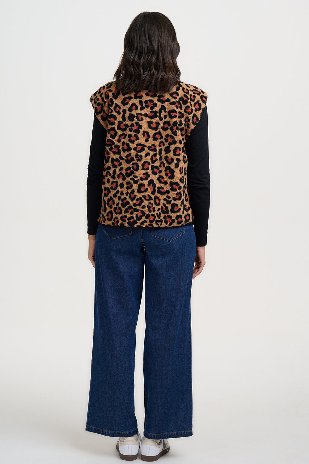 Person wearing a leopard print vest, black long-sleeve shirt, and blue jeans on a white background