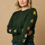 A woman wearing a green crew neck jumper with multicolored star intarsia sleeves, paired with blue jeans.