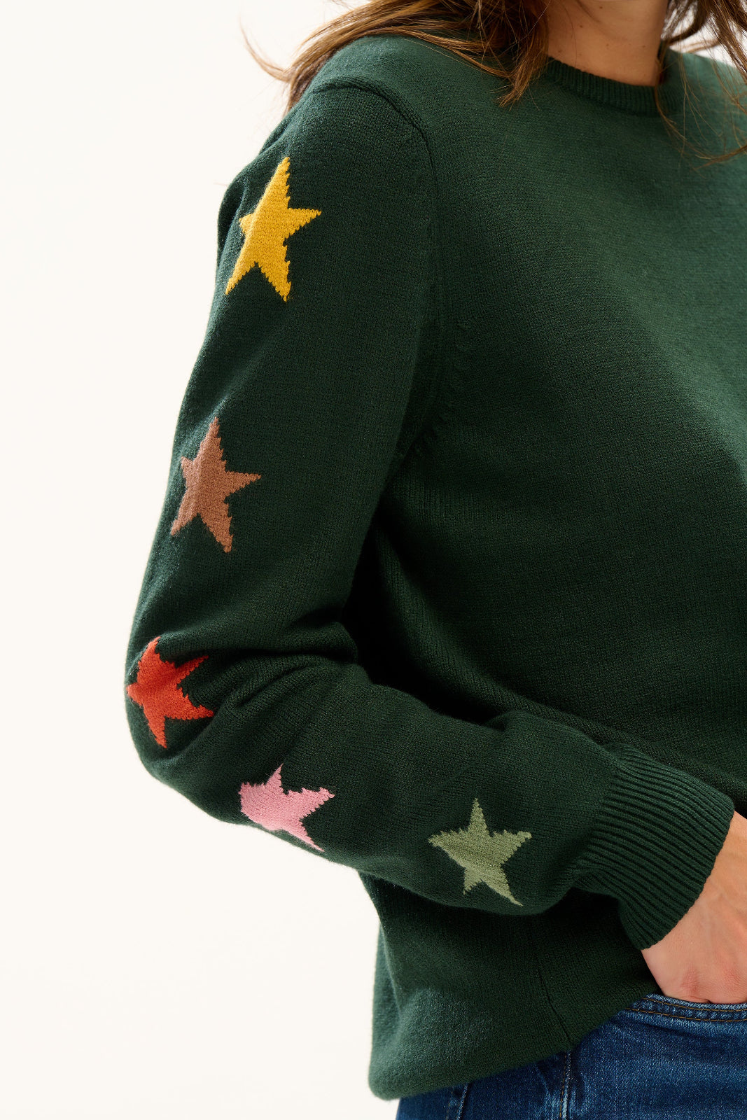 Green sweater with colorful star patterns worn by a person on a white background