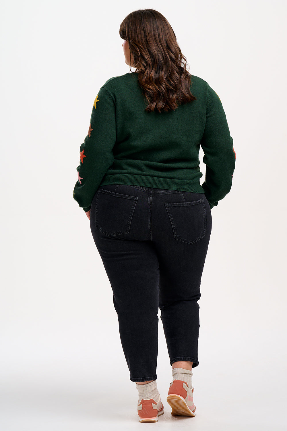 Person wearing a green sweatshirt with colorful sleeves and blue jeans on a white background