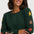 A woman wearing a dark green crewneck sweater with colorful star patterns in yellow, orange, and green, posed against a light gray background.