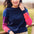 A woman wearing a navy crew neck jumper with color block sleeves in pink and purple, paired with beige pants, standing outdoors.