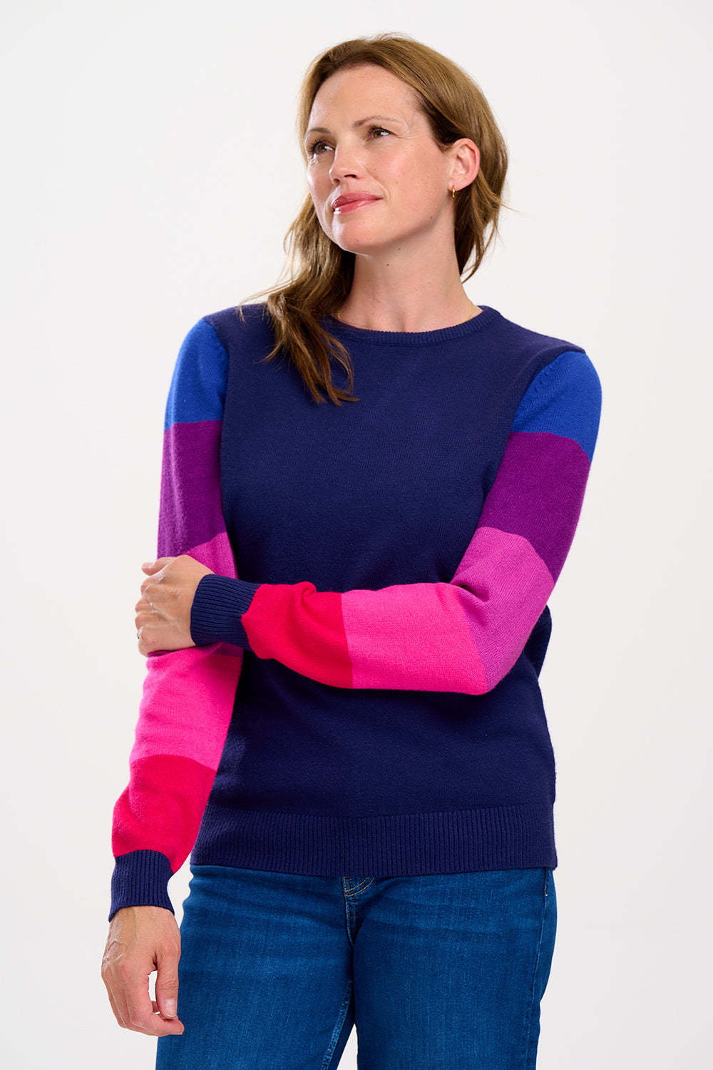 A woman wearing a navy crew neck jumper with colour block sleeves in pink and purple, paired with jeans. 