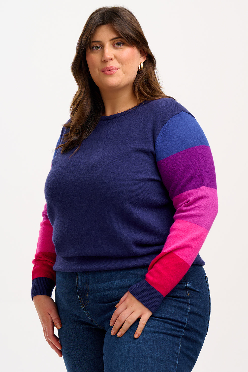 A woman wearing a navy crew neck jumper with colour block sleeves in pink and purple, paired with jeans. 