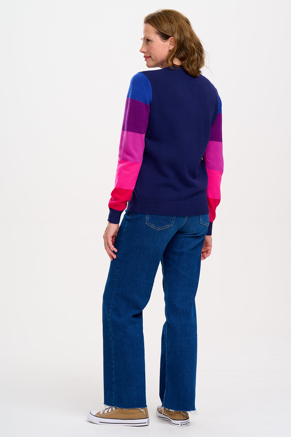 A woman wearing a navy crew neck jumper with colour block sleeves in pink and purple, paired with jeans. 