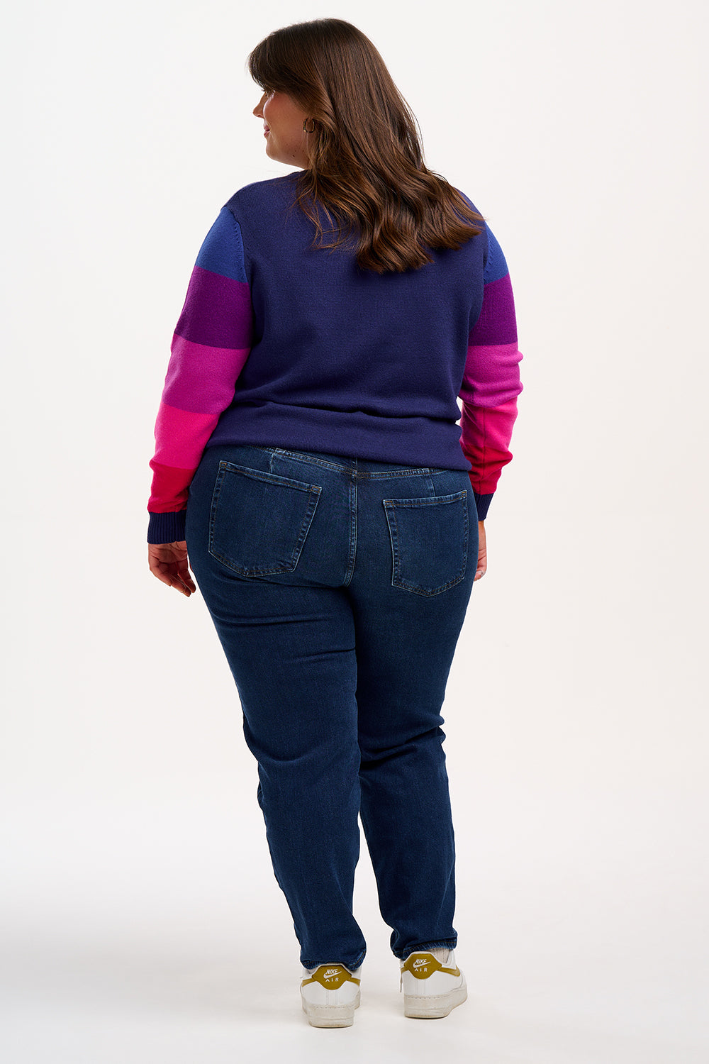 A woman wearing a navy crew neck jumper with colour block sleeves in pink and purple, paired with jeans. 