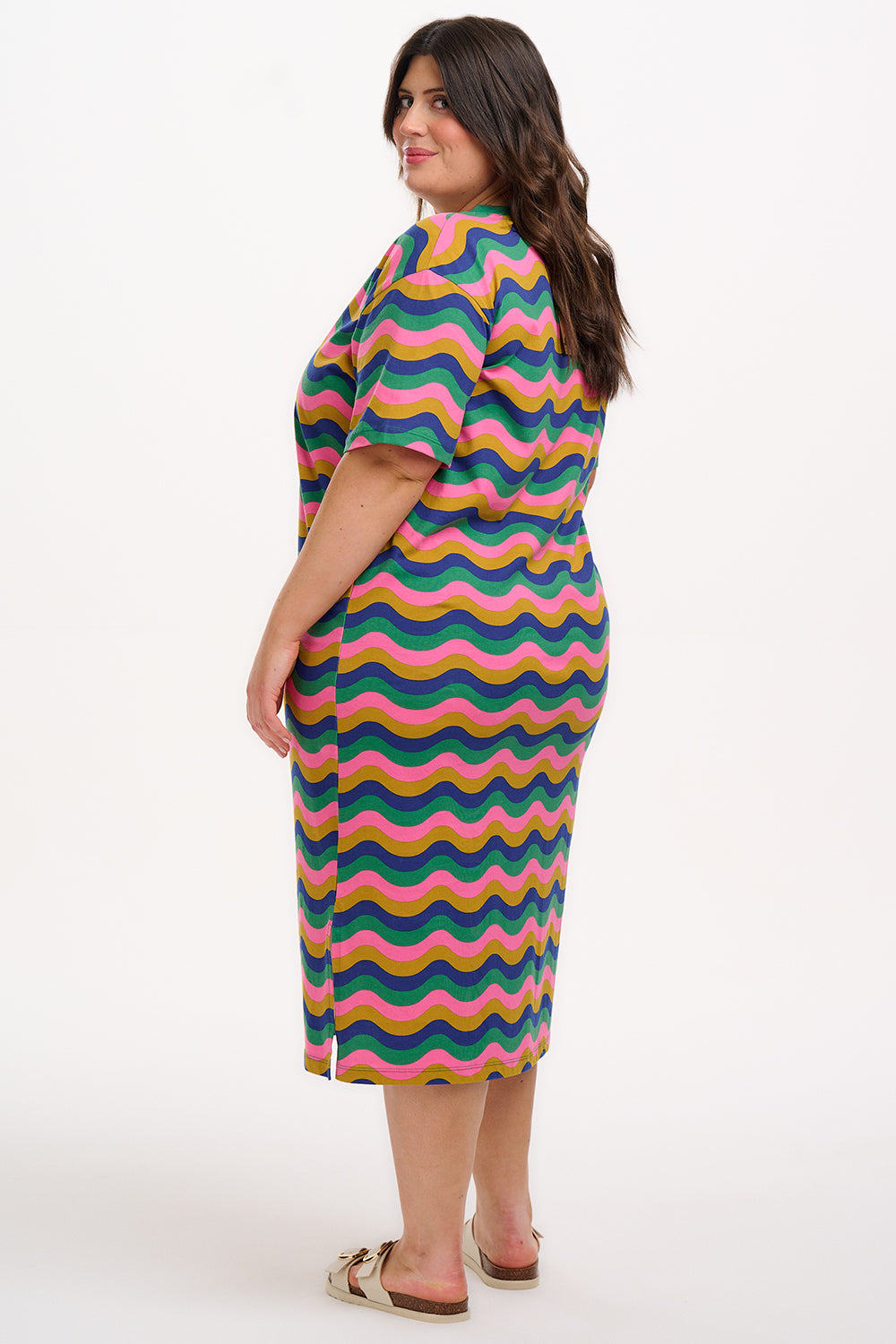 A model wearing a midi t-shirt dress with a multicolor rainbow waves print. The dress is knee-length, has a ribbed collar, and short sleeves.