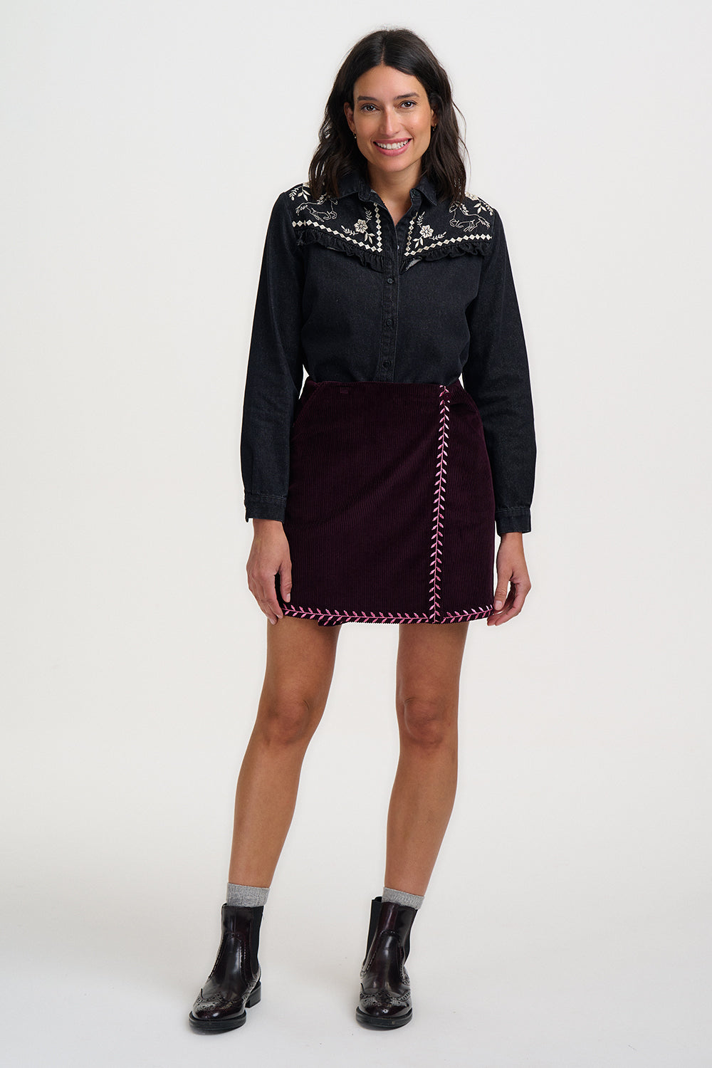 Woman wearing a black embroidered blouse and skirt with black boots on a white background