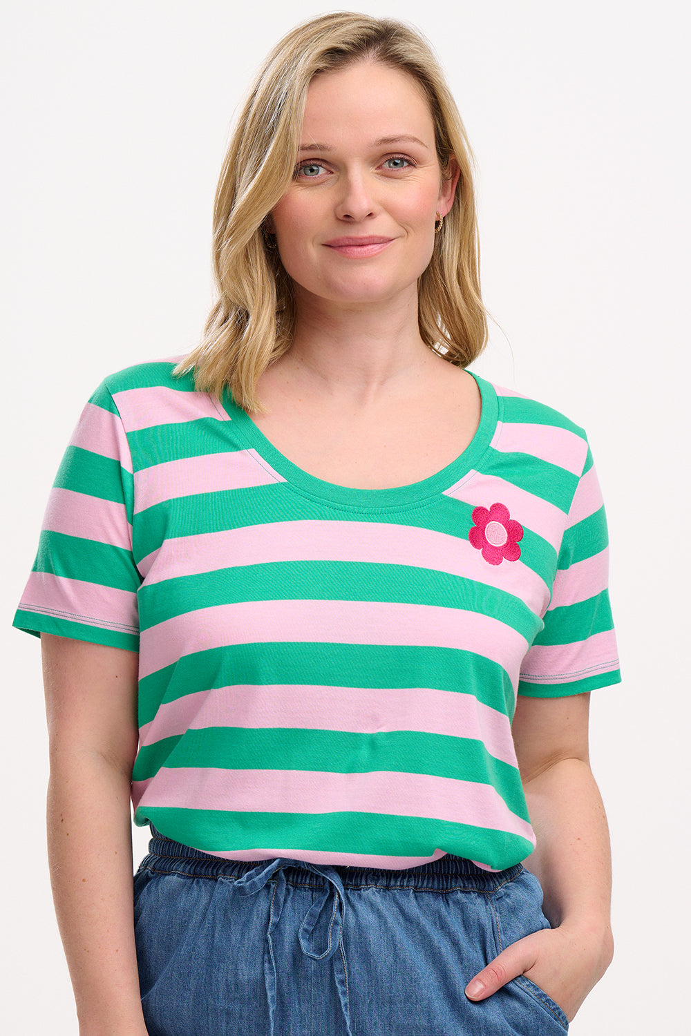 A woman wearing a green and pink striped scoop neck t-shirt with a flower detail on the chest.