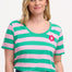 A woman wearing a green and pink striped scoop neck t-shirt with a flower detail on the chest.
