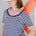 A woman wearing a striped scoop neck t-shirt in white and navy colors with a small floral design on the chest, paired with a white cap and dark shorts.