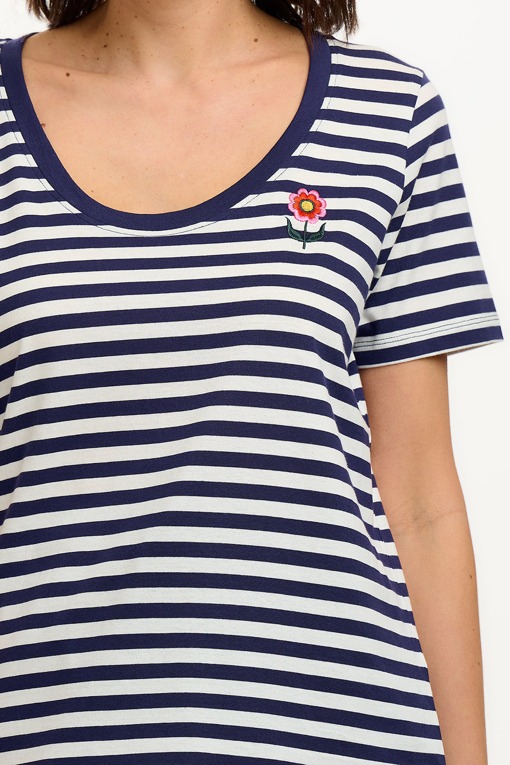 A woman wearing a striped scoop neck t-shirt in white and navy colors with a small floral design on the chest