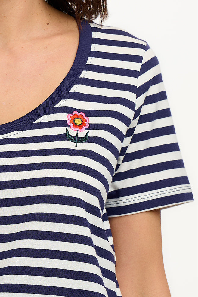 A woman wearing a striped scoop neck t-shirt in white and navy colors with a small floral design on the chest