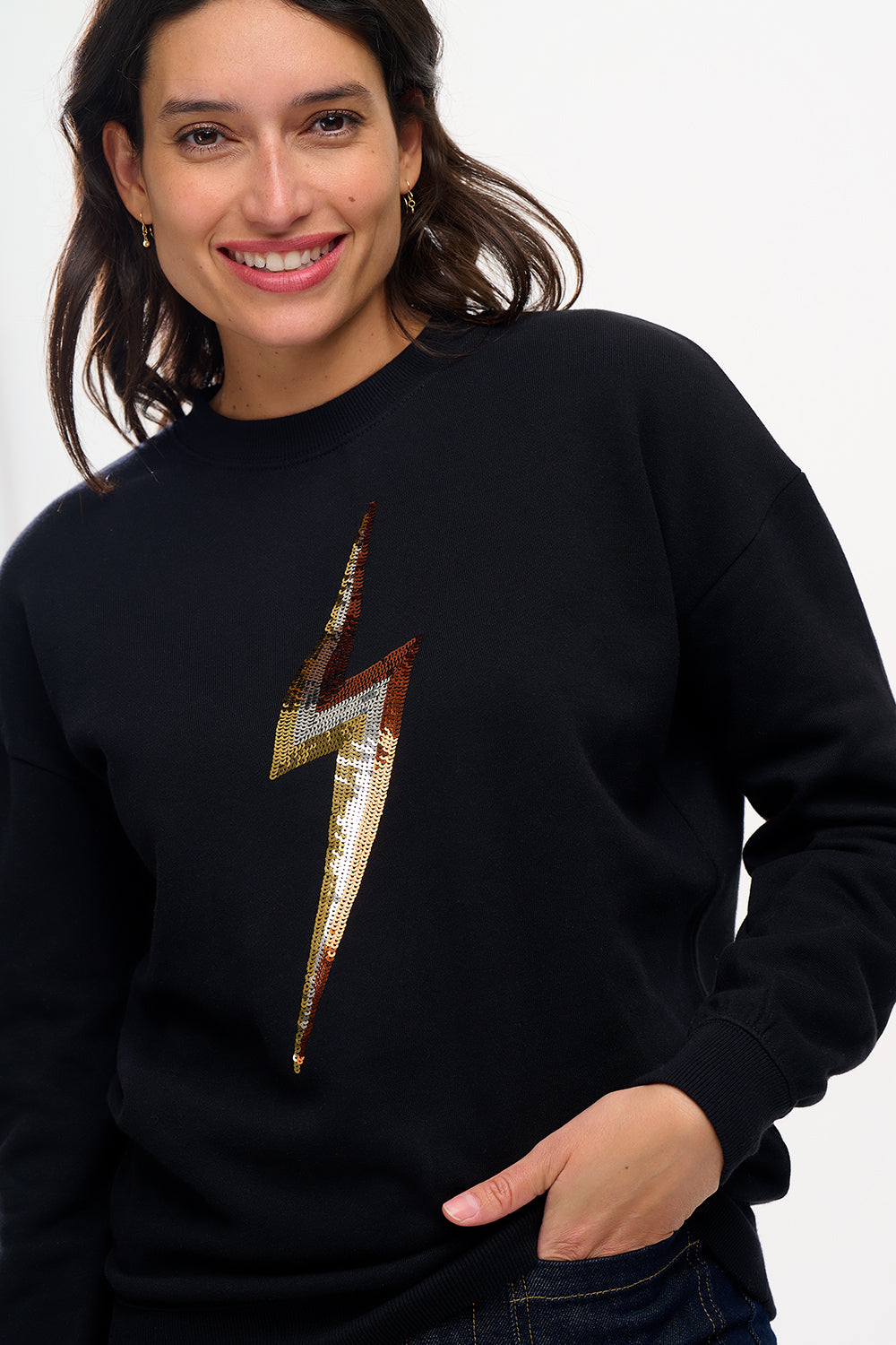 A woman smiling and wearing a black sweatshirt with a sequin lightning bolt design on the front.